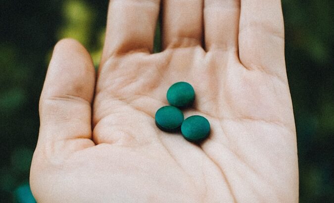 a hand holding two green pills in it's palm